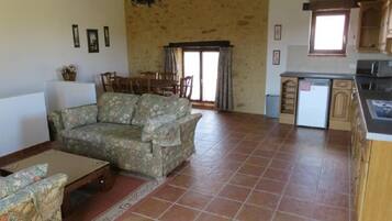 A living room with a sofa, a dining table, and chairs, a kitchen with cabinets and a refrigerator, and a stone wall.