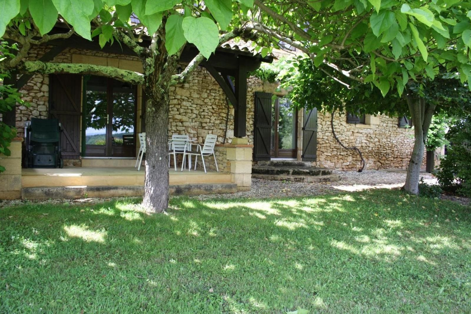 A stone building with a covered patio, outdoor seating, and a tree in the foreground.