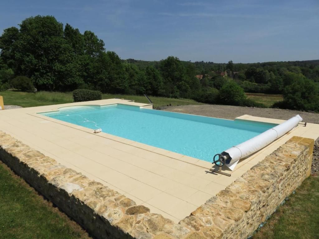A rectangular swimming pool with a stone border, surrounded by a grassy area and trees.
