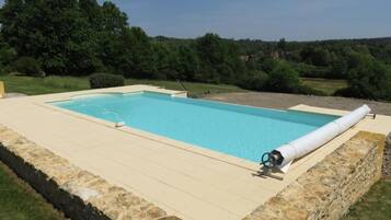 A rectangular swimming pool with a stone border, surrounded by a grassy area and trees.