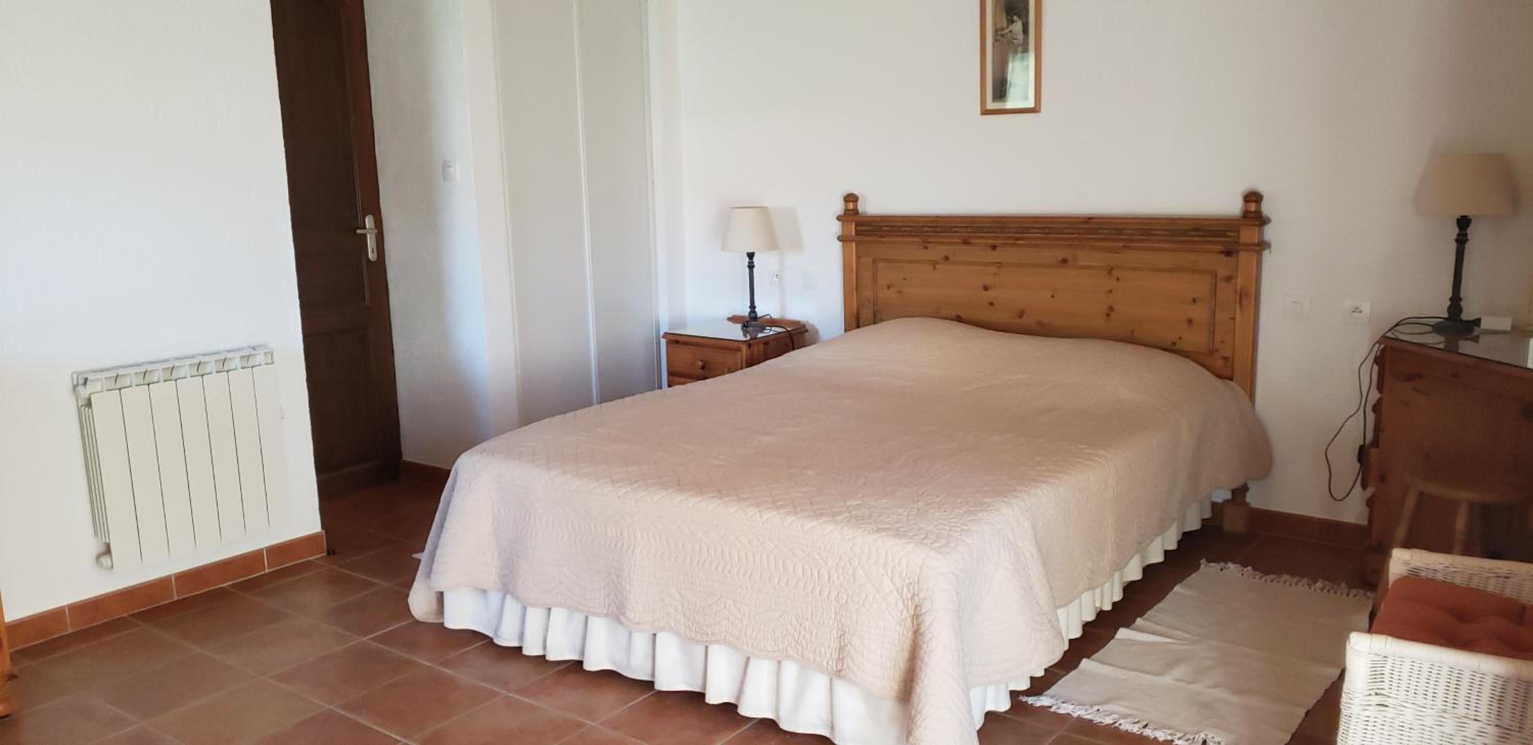 A bedroom with a bed, a nightstand, a lamp, a radiator, and a chair.