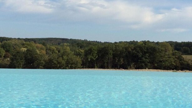 A clear blue swimming pool with a view of a forested hill under a partly cloudy sky. - Domaine de Manilau - B&B (Le Buisson-de-Cadouin)