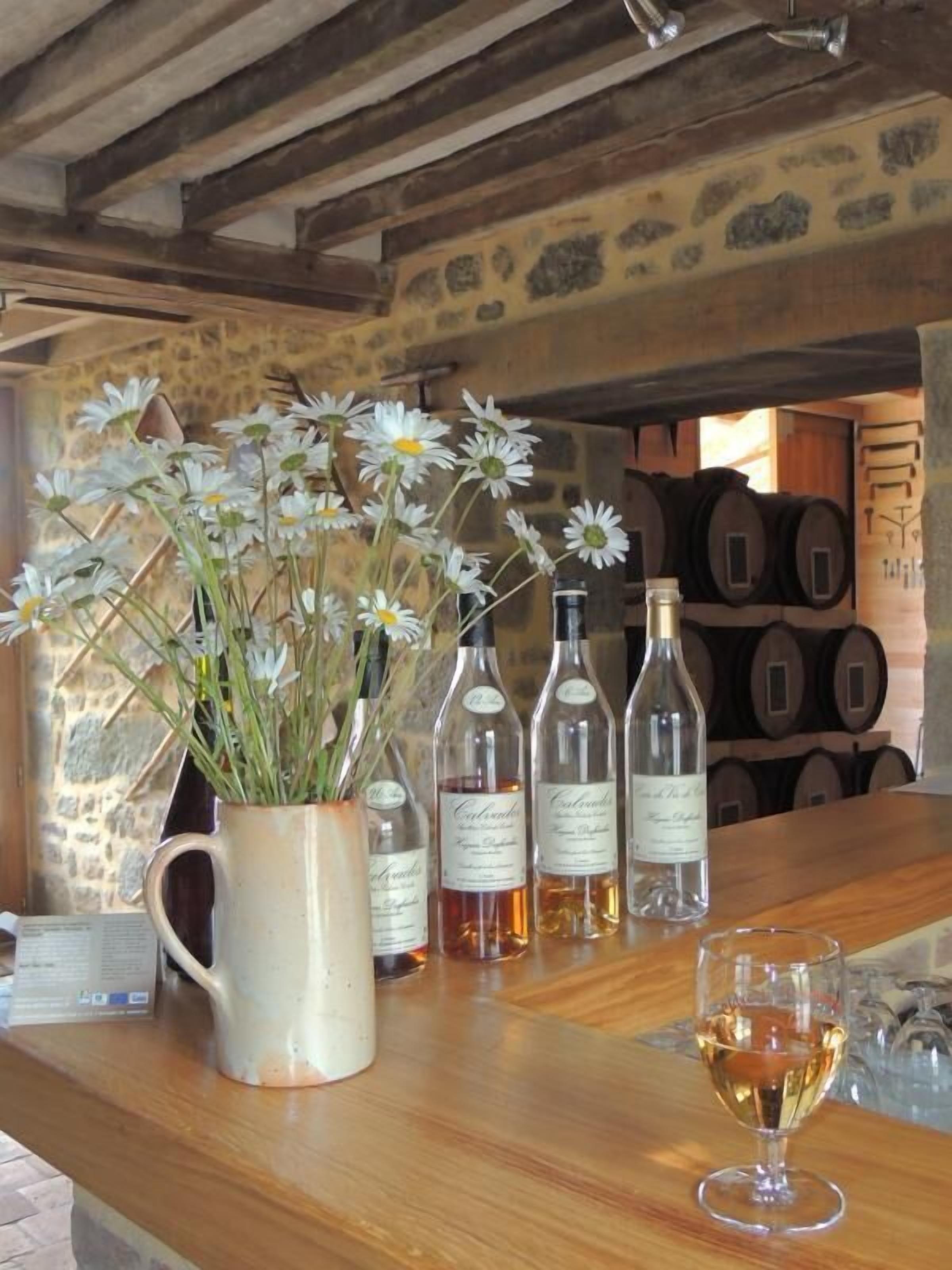 Um espaço de bar rústico com balcão de madeira, um vaso de flores brancas e algumas garrafas de vinho.