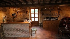 A rustic kitchen with a brick island, wooden shelves, and a large window. - Ferme Cidricole Hugues Desfrièches (Sainte-Marguerite-de-Carrouges)