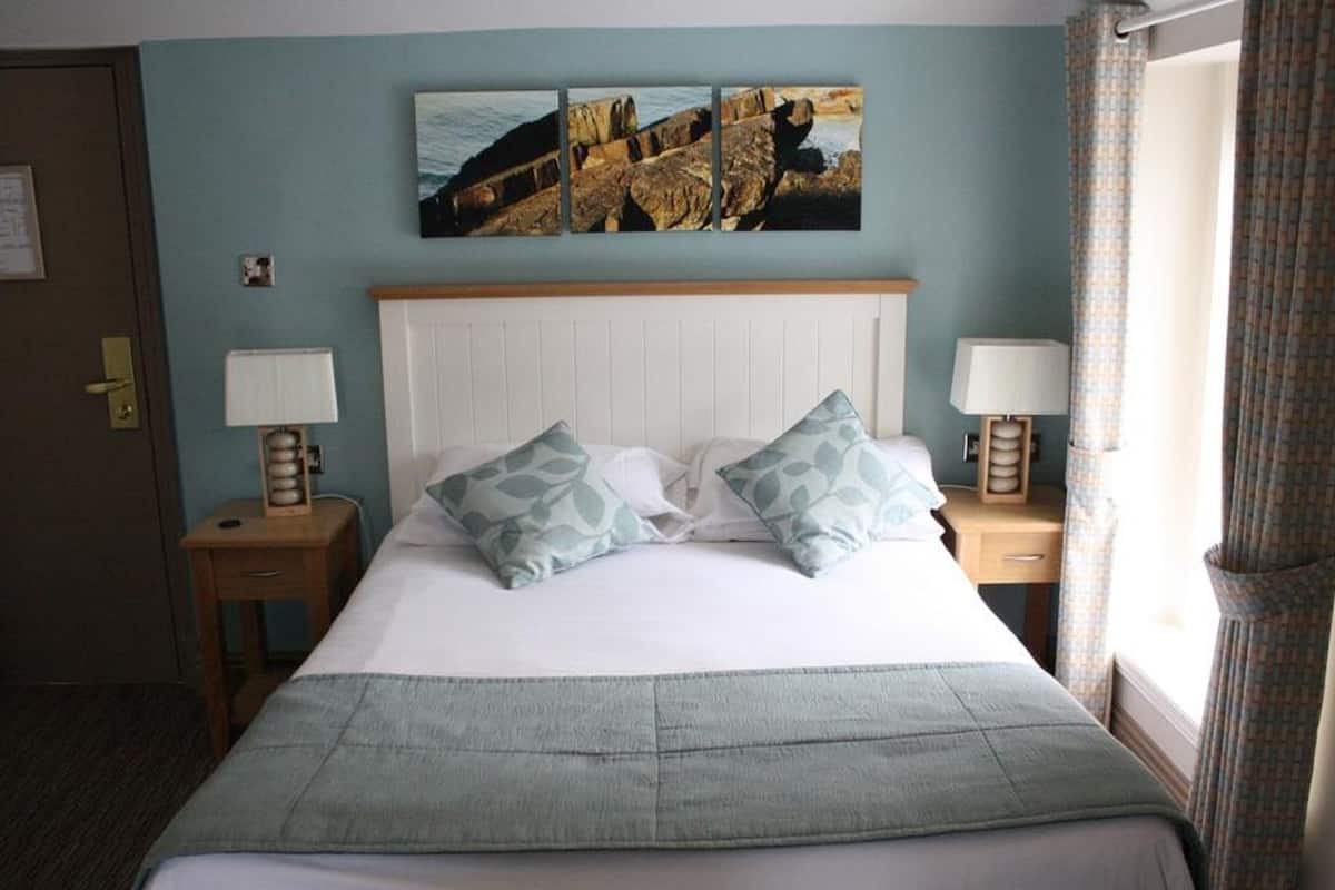 Quarto de hotel com cama, duas mesas de cabeceira, uma janela com cortinas e parede decorada com três quadros.