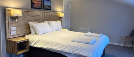 A modern bedroom with a large bed, wooden headboard, bedside lamps, and a small wooden nightstand.
