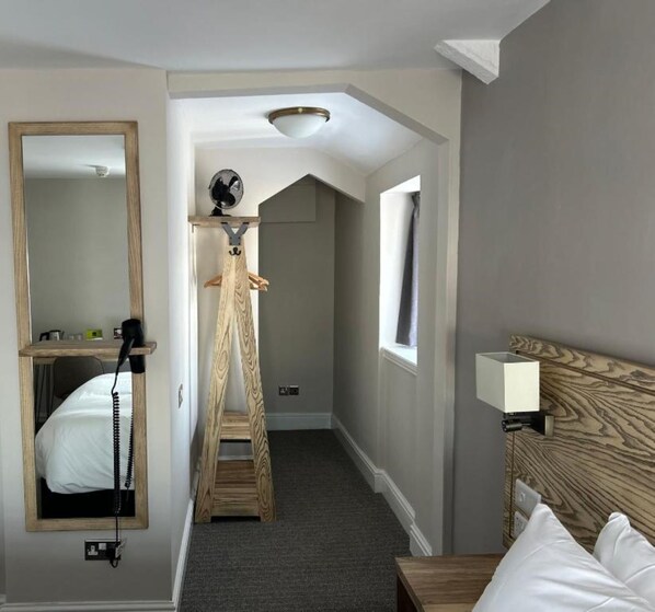 A hotel room with a wooden ladder, a bed, a bedside table, a mirror, and a window.