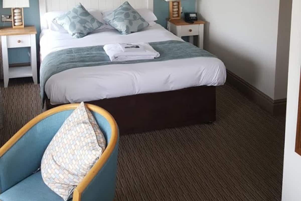 Quarto de hotel com cama, duas mesas de cabeceira com abajures, uma cadeira e obras de arte nas paredes.