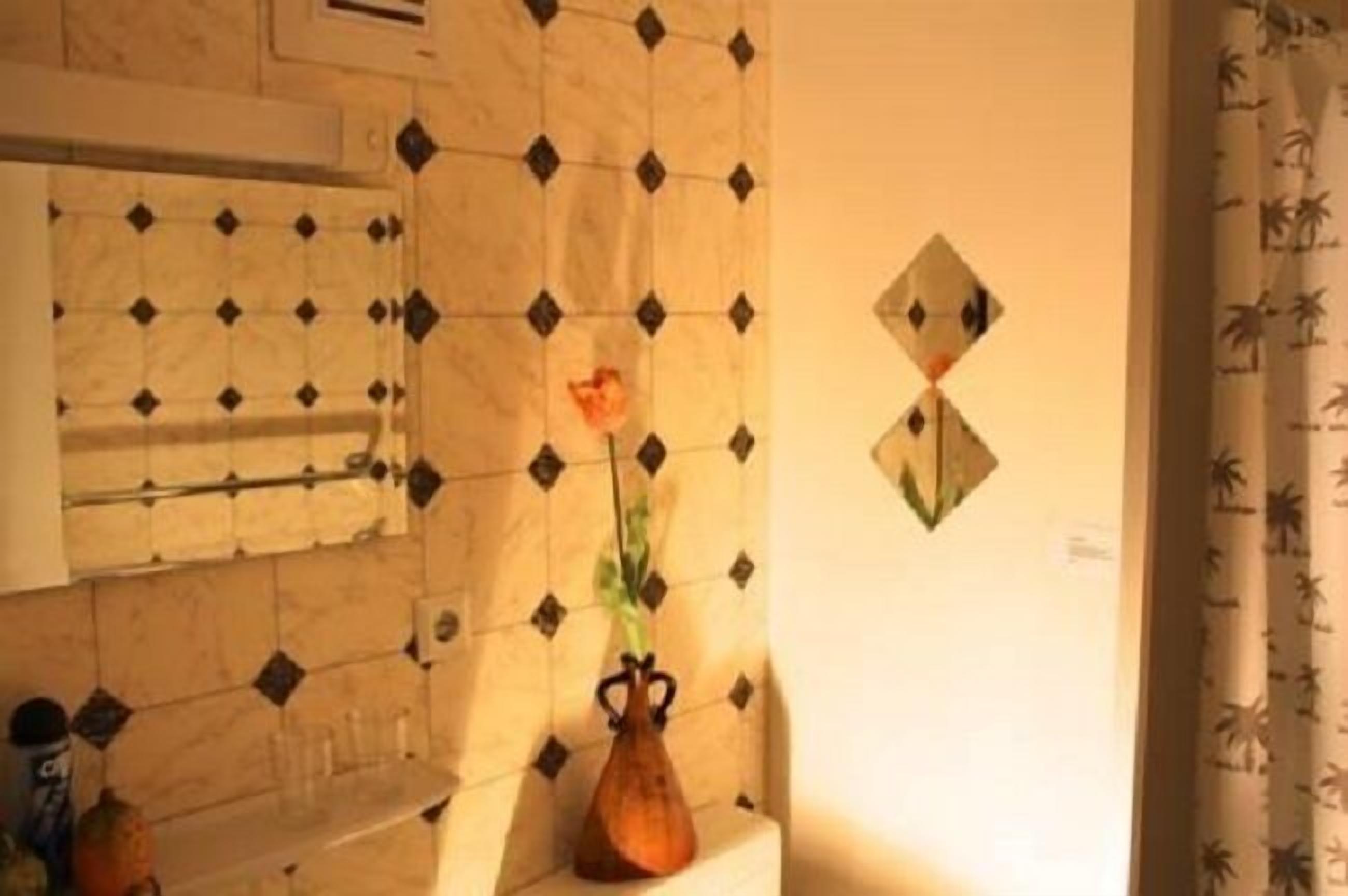 Casa de banho com parede revestida de azulejos, um vaso com uma flor e um porta-toalhas.