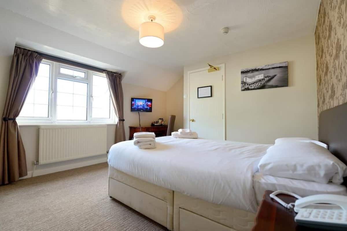 A hotel room with a large bed, a television, a desk with a telephone, and a door with a framed picture.