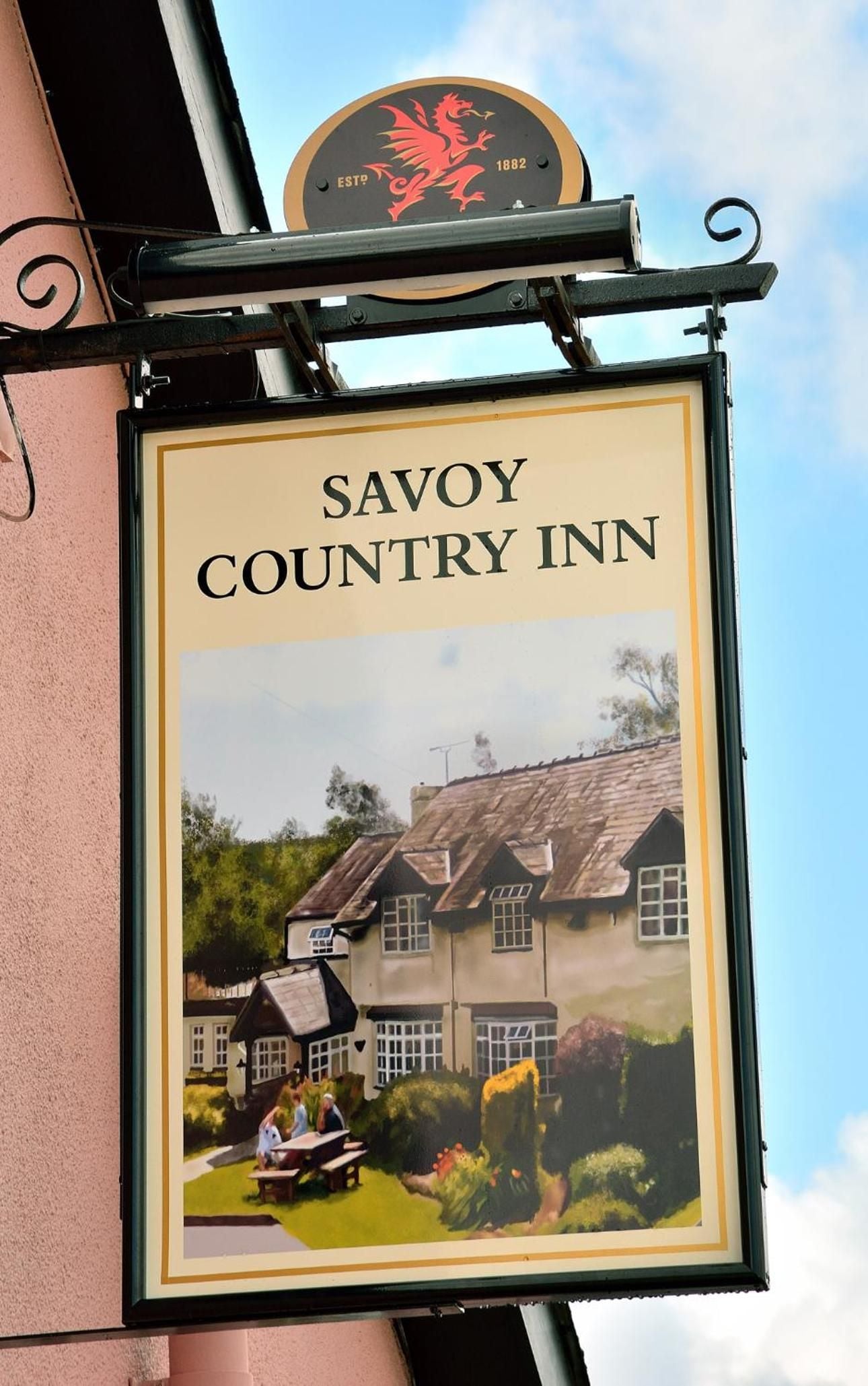 Señal para Savoy Country Inn con una representación de un edificio tradicional y una pequeña mesa con gente.