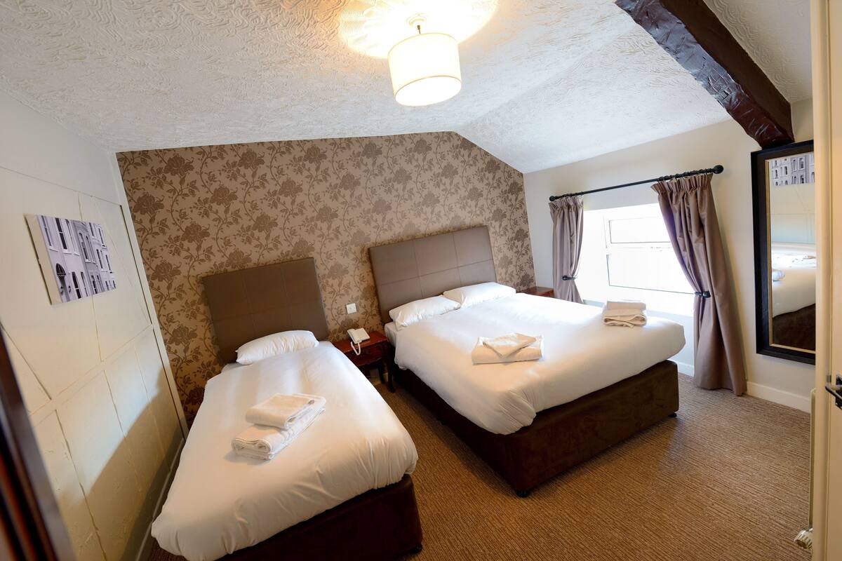A hotel room with two beds, a headboard, a nightstand, and a window with curtains.