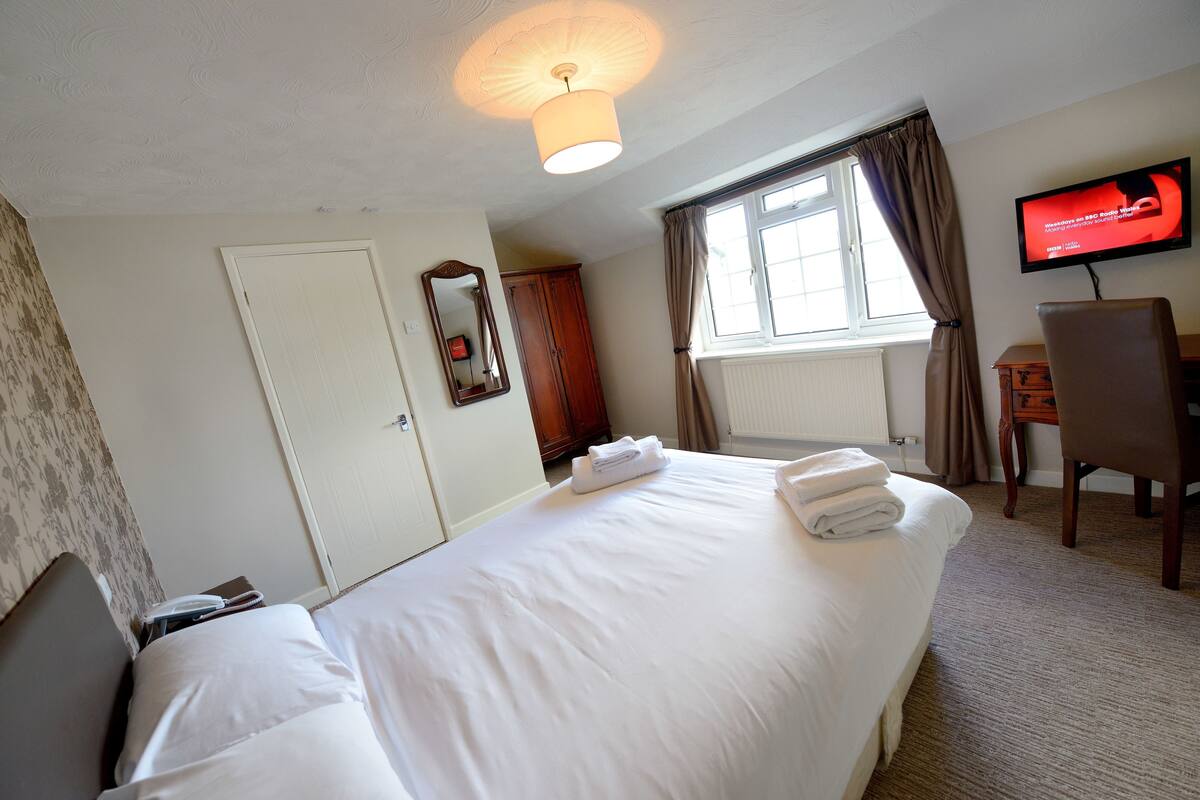 A hotel room with a bed, a television, a desk, and a window with curtains.