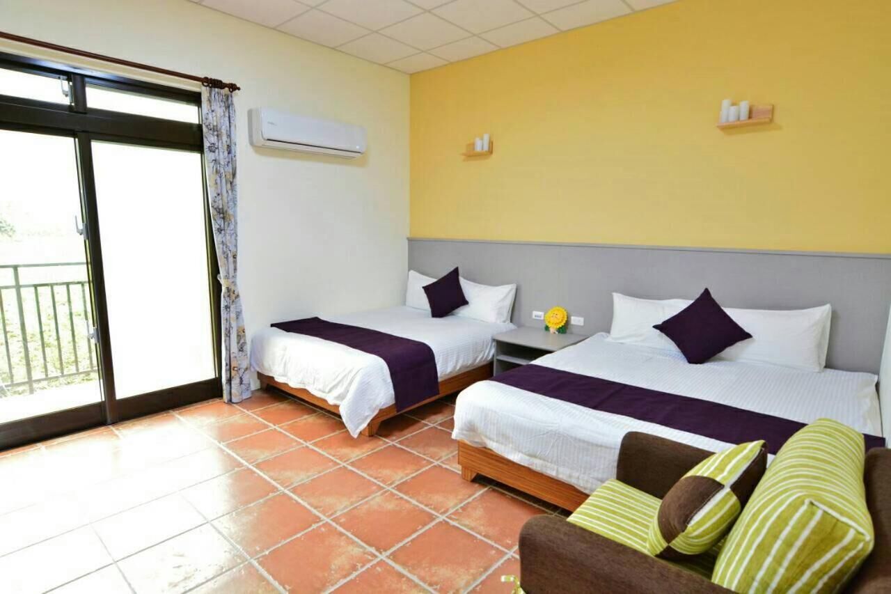 A hotel room with two beds, a sofa, a balcony, and a yellow wall.