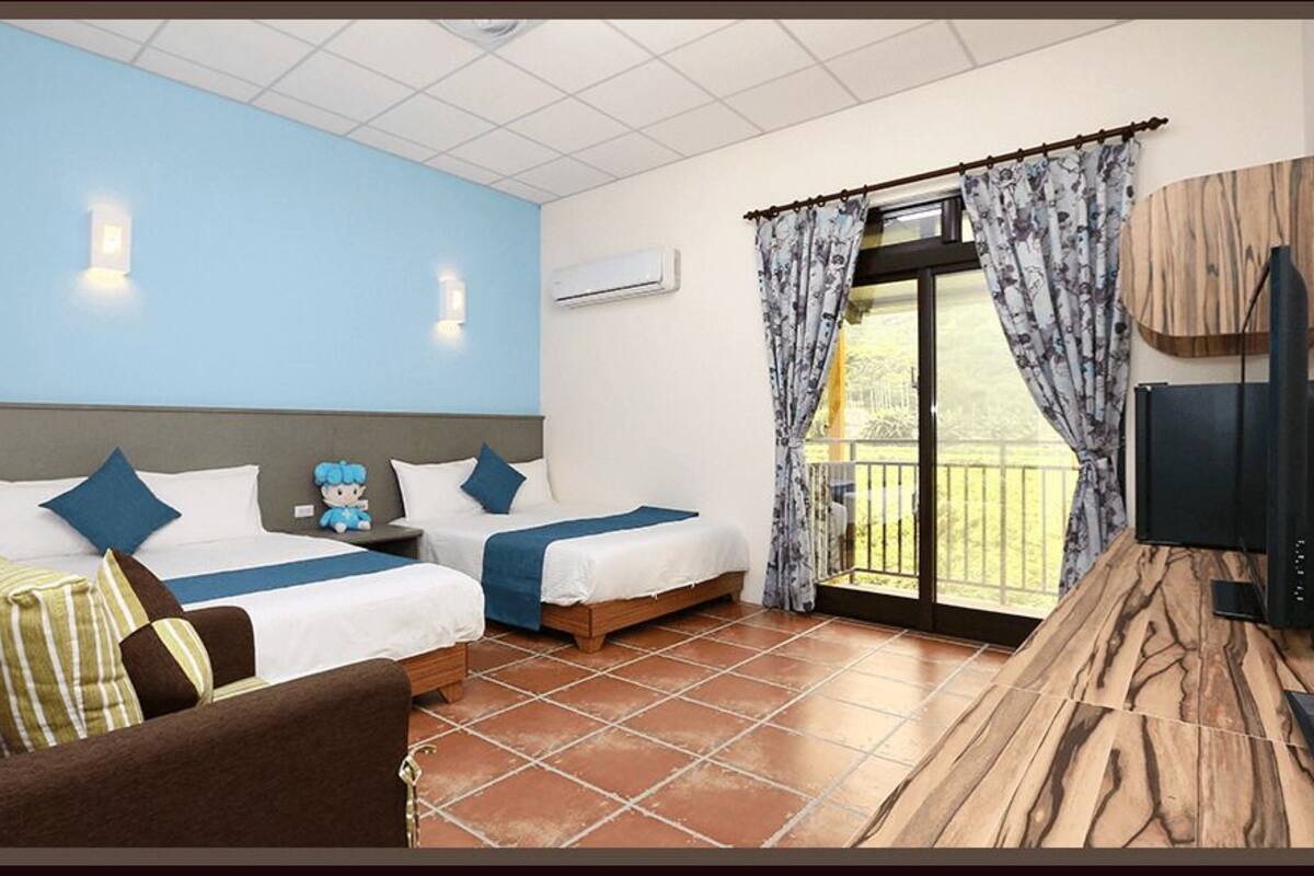A hotel room with two beds, a sofa, a TV, and a balcony with curtains.