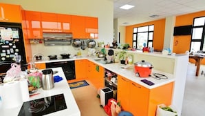 Une cuisine avec des meubles de rangement orange, une cuisinière et divers ustensiles de cuisine.