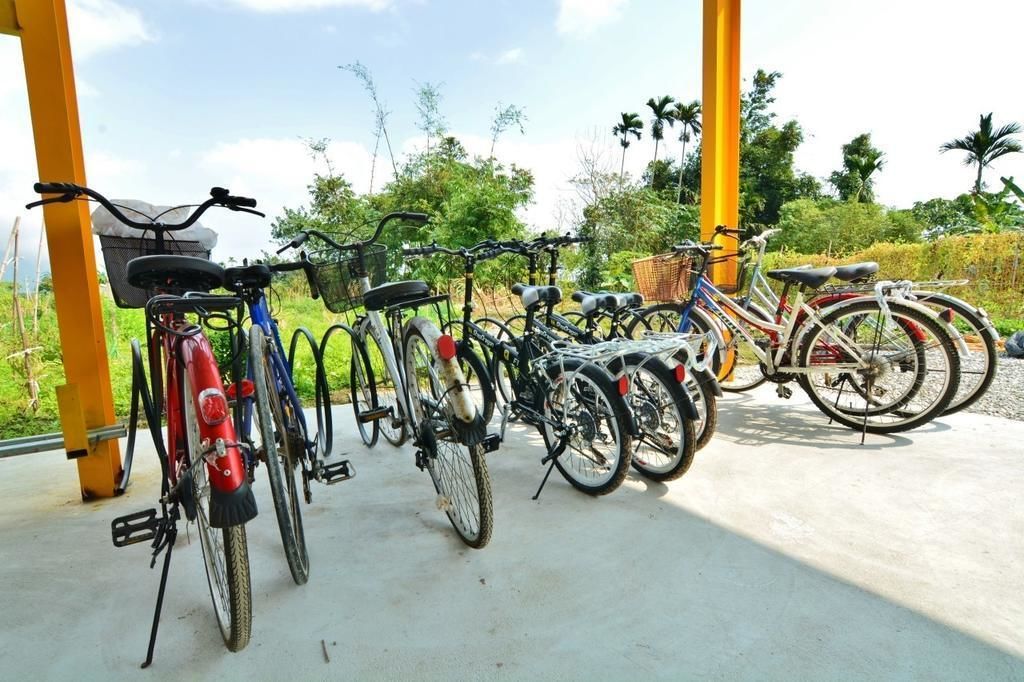 A row of bicycles parked under a structure with a view of greenery and trees in the background.