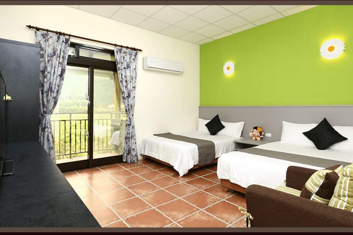 A hotel room with two beds, a sofa, a balcony with curtains, and a green wall with a sun decoration.