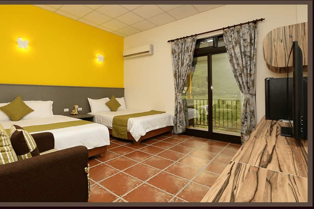 A hotel room with two beds, a sofa, a TV, and a balcony with curtains.