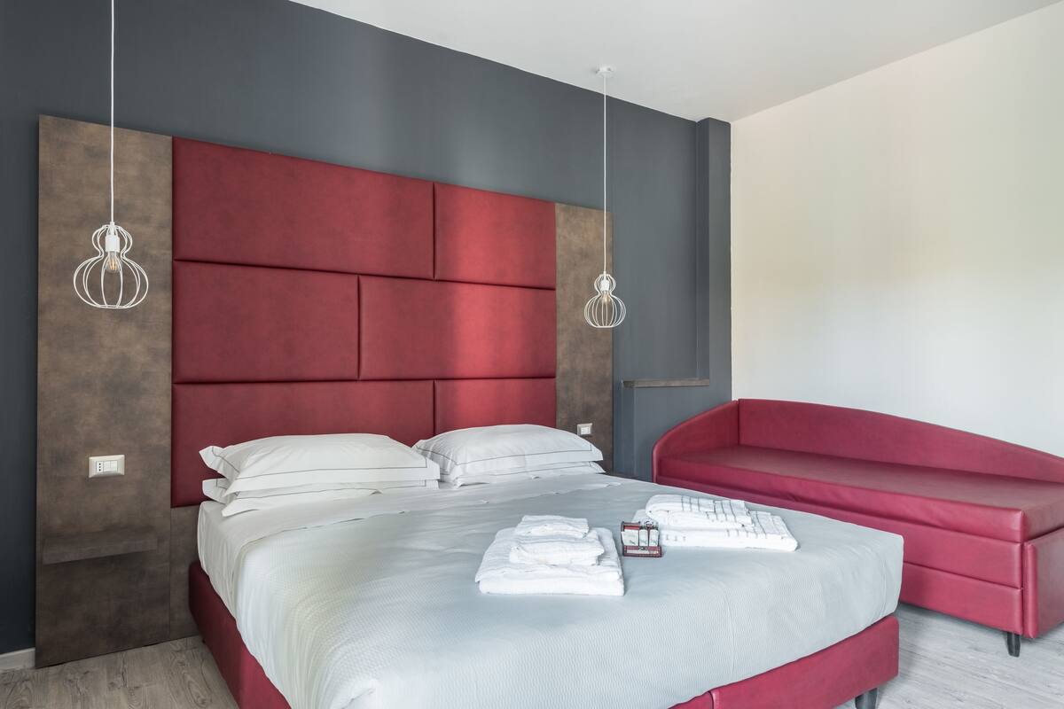 Un dormitorio moderno con una cama grande, un sofá rojo y dos lámparas colgantes.