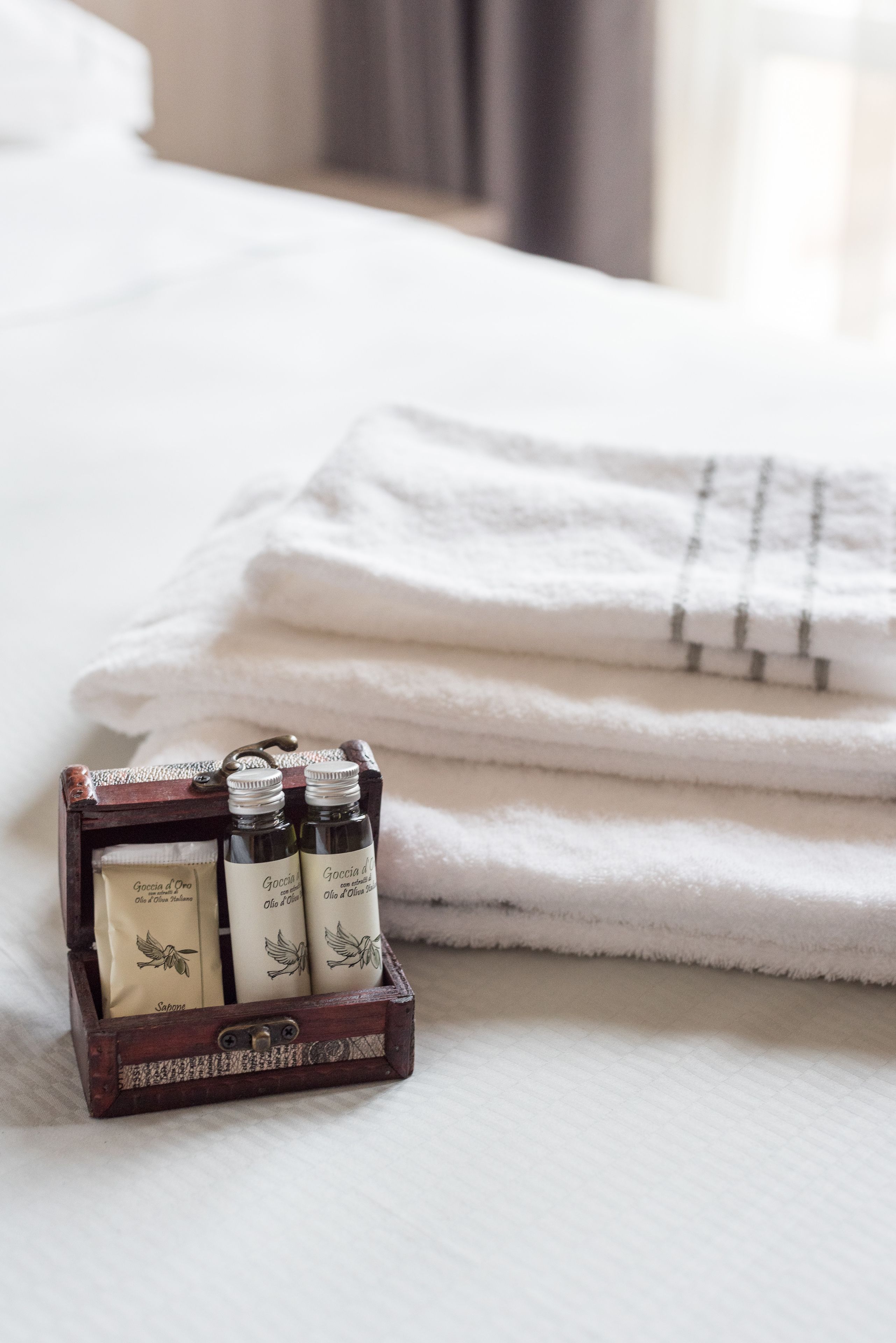 A neatly folded white towel and a wooden box with three bottles of toiletries on a bed.