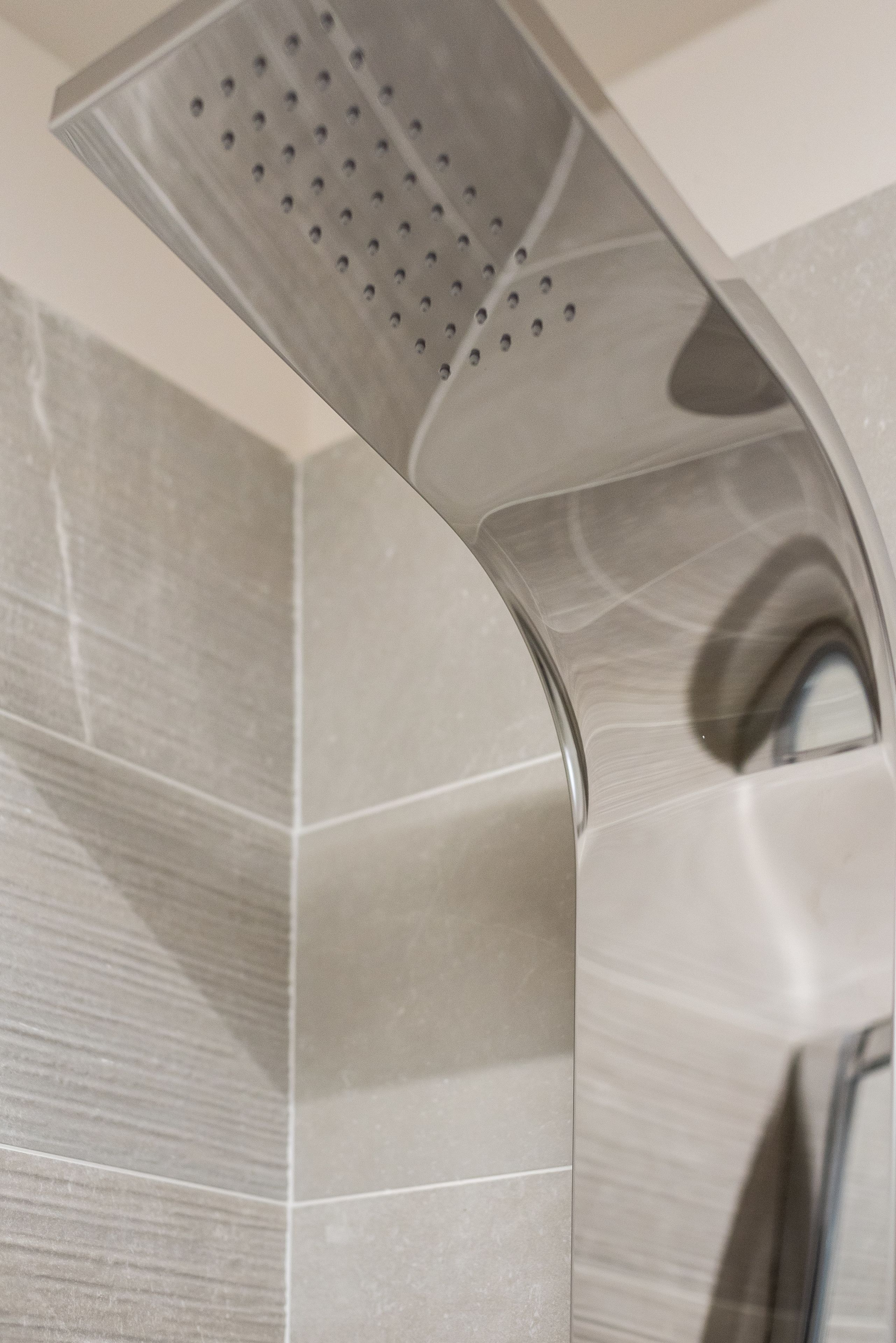 Un pommeau de douche au design incurvé et doté de plusieurs orifices, fixé sur un mur dont la surface est recouverte de carreaux.