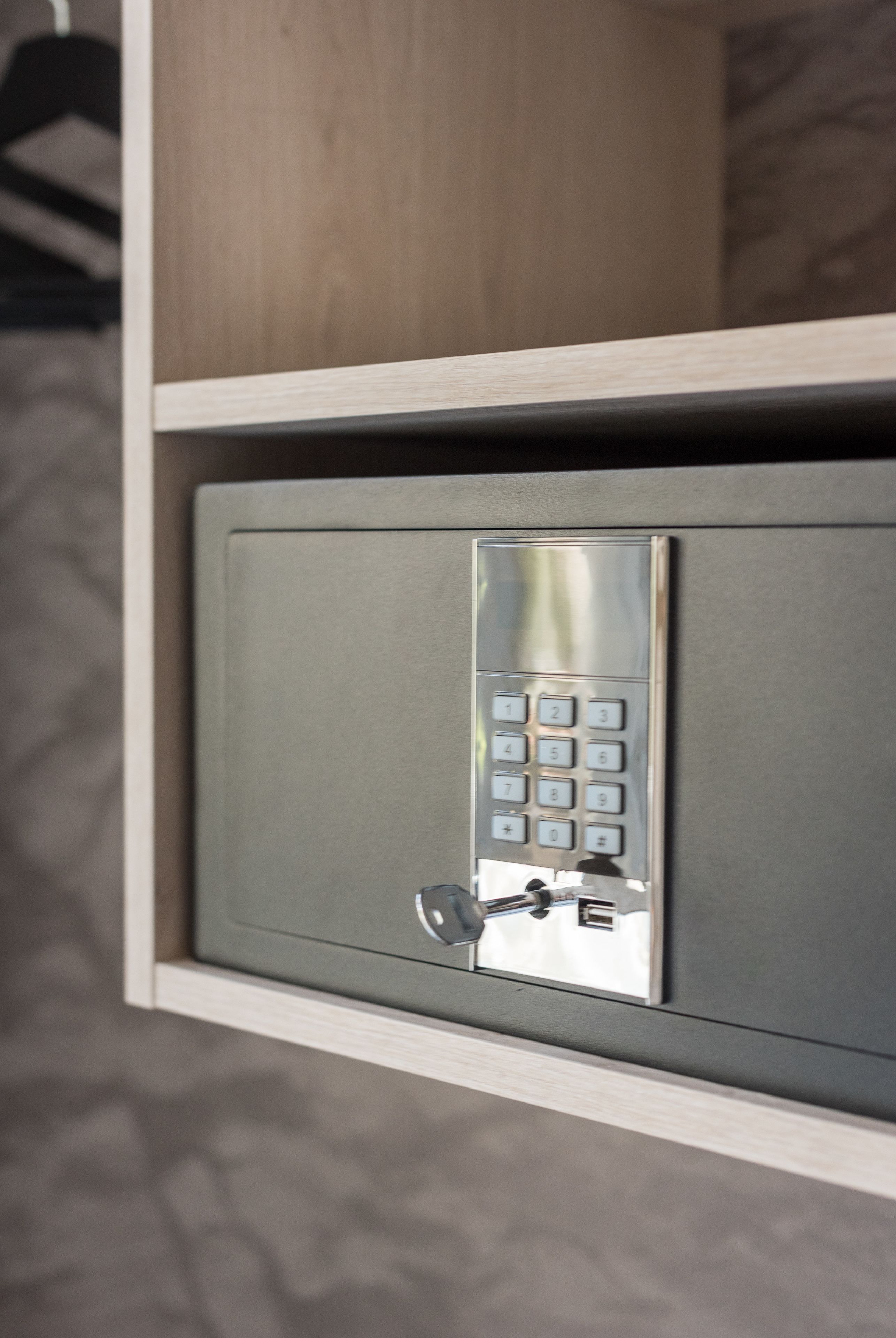 A metal safe with a keypad lock, mounted on a wall with a wooden panel above.