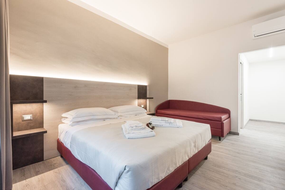 Una habitación de hotel moderna con una cama grande, un sofá rojo y un cabecero empotrado.