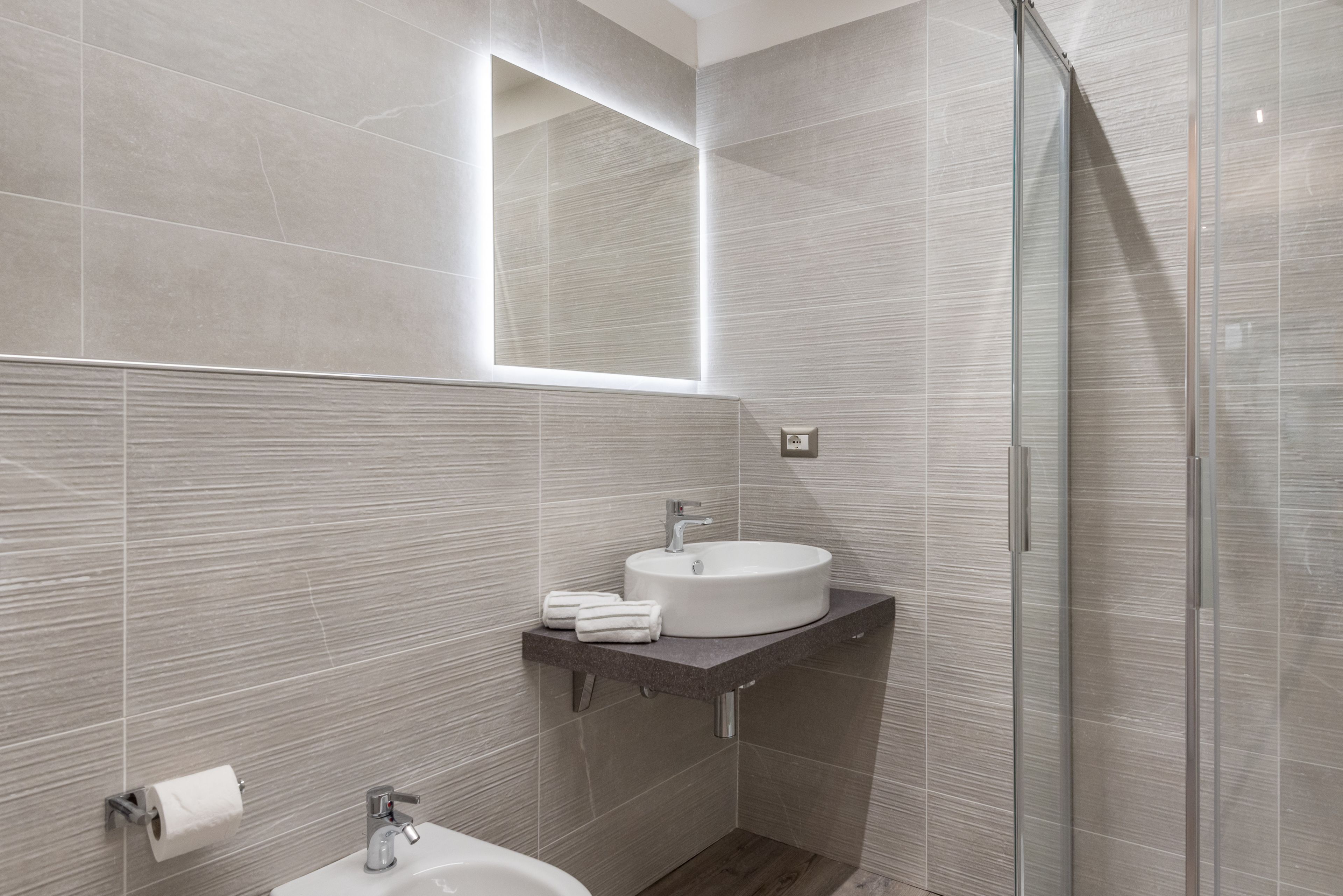 A modern bathroom with a large mirror, a sink, and a shower.