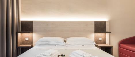 A neatly made bed with white linens, two bedside tables with lamps, and a red chair.