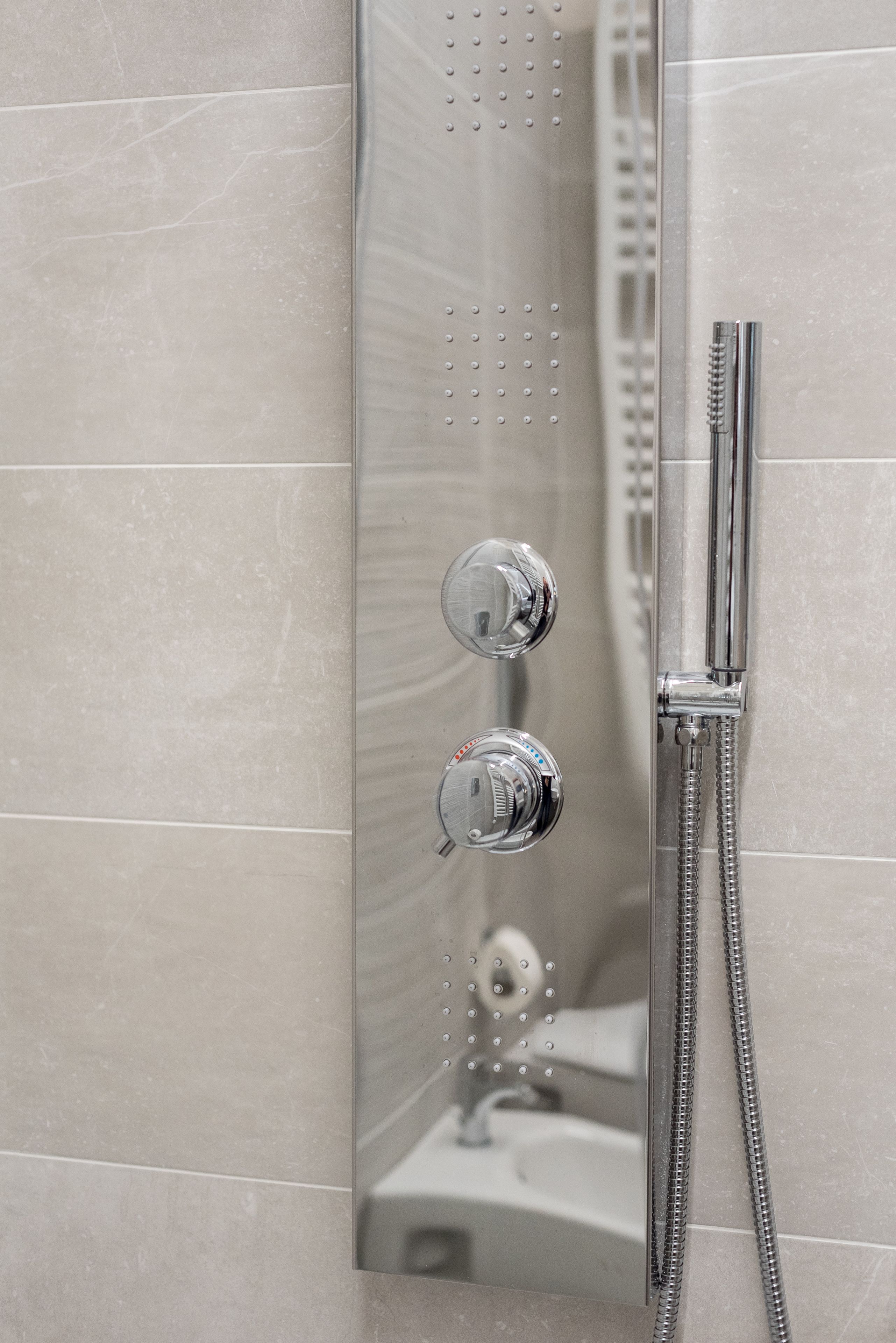 A bathroom with a shower enclosure, a handheld showerhead, and a control knob.