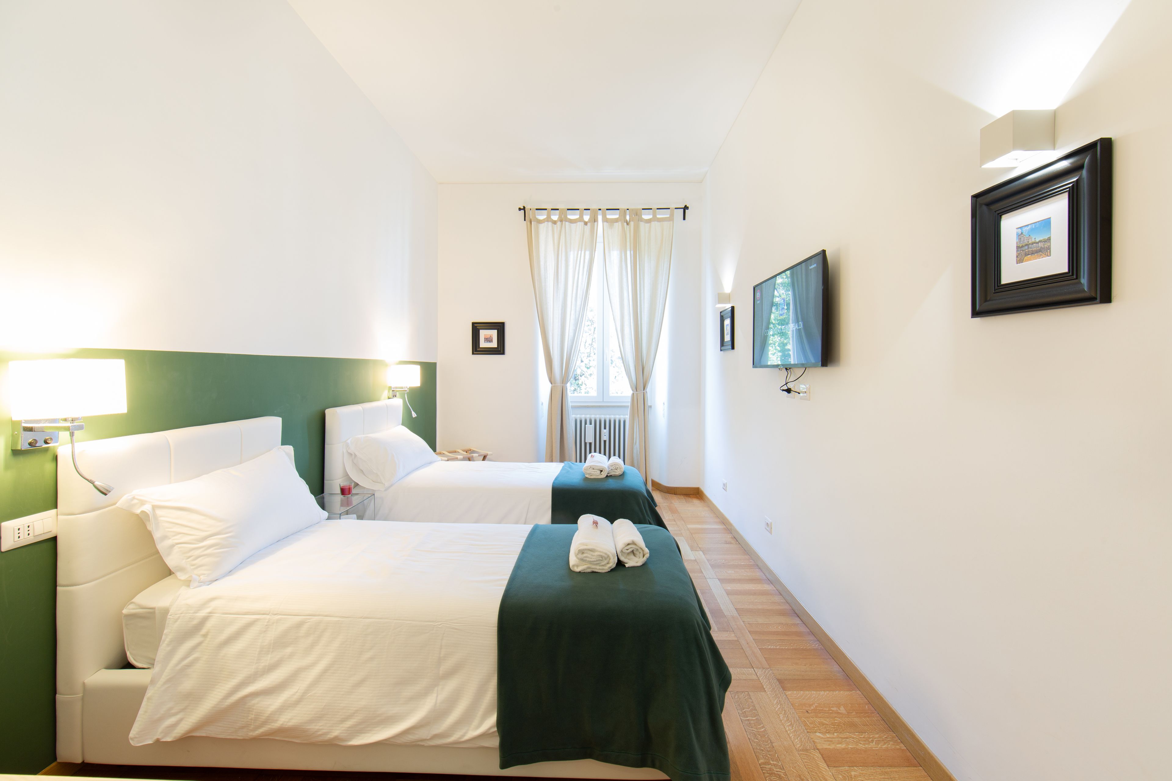 A hotel room with two beds, a television, and a window with curtains.