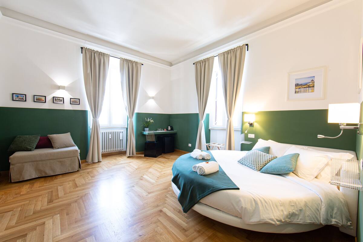A hotel room with a large bed, a sofa, a desk, and a window with curtains.