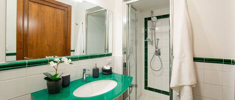 A bathroom with a green sink, a mirror, a wooden cabinet, and a glass shower enclosure.