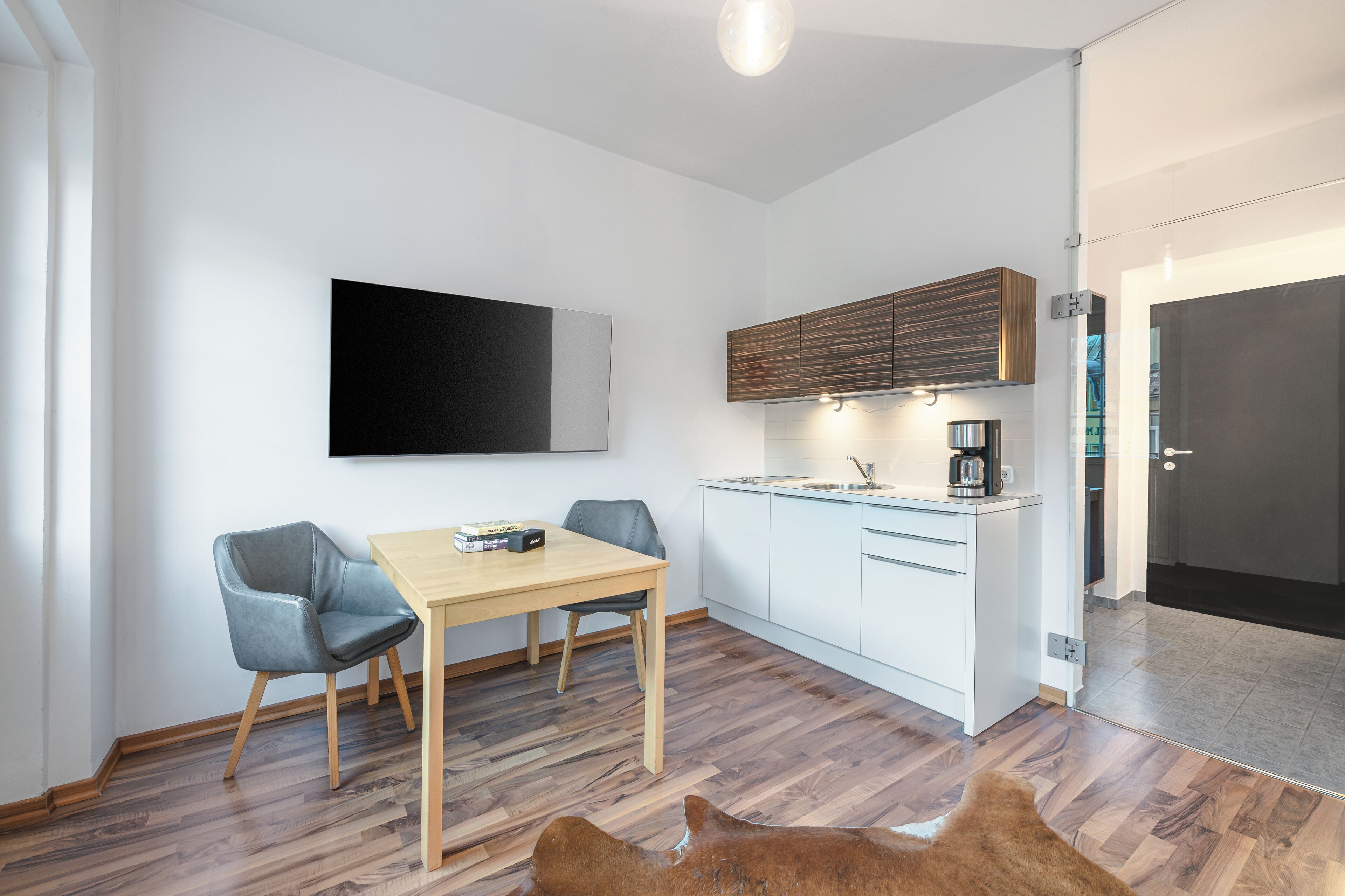 A modern kitchen with a wooden table and chairs, a flat-screen TV, and a coffee machine.