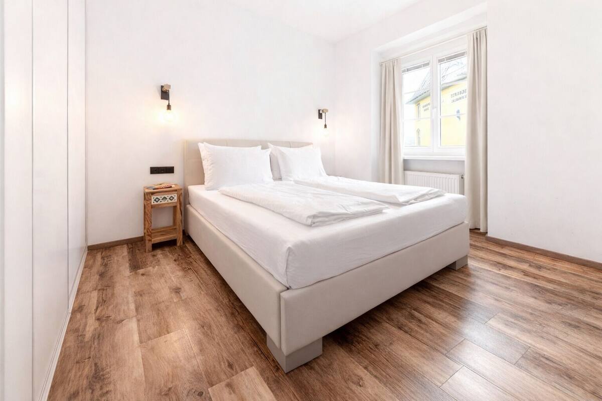 Ein schlicht eingerichtetes Schlafzimmer mit einem großen Bett, Holzboden und zwei Wandleuchten.