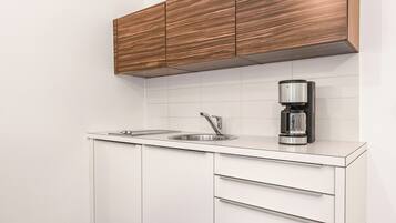 A modern kitchen with white cabinetry, a wooden floor, and a coffee maker on the countertop.