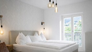 A bedroom with a large bed, a wooden nightstand, a woven chair, and a view of the outdoors through a sliding glass door. - Club Alpenresidenz Bad Gastein (Bad Gastein)
