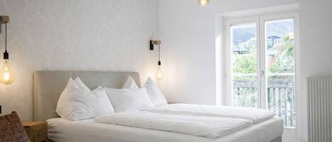 Een slaapkamer met een groot bed, een houten nachtkastje, een geweven stoel en uitzicht op het landschap door een schuifdeur.