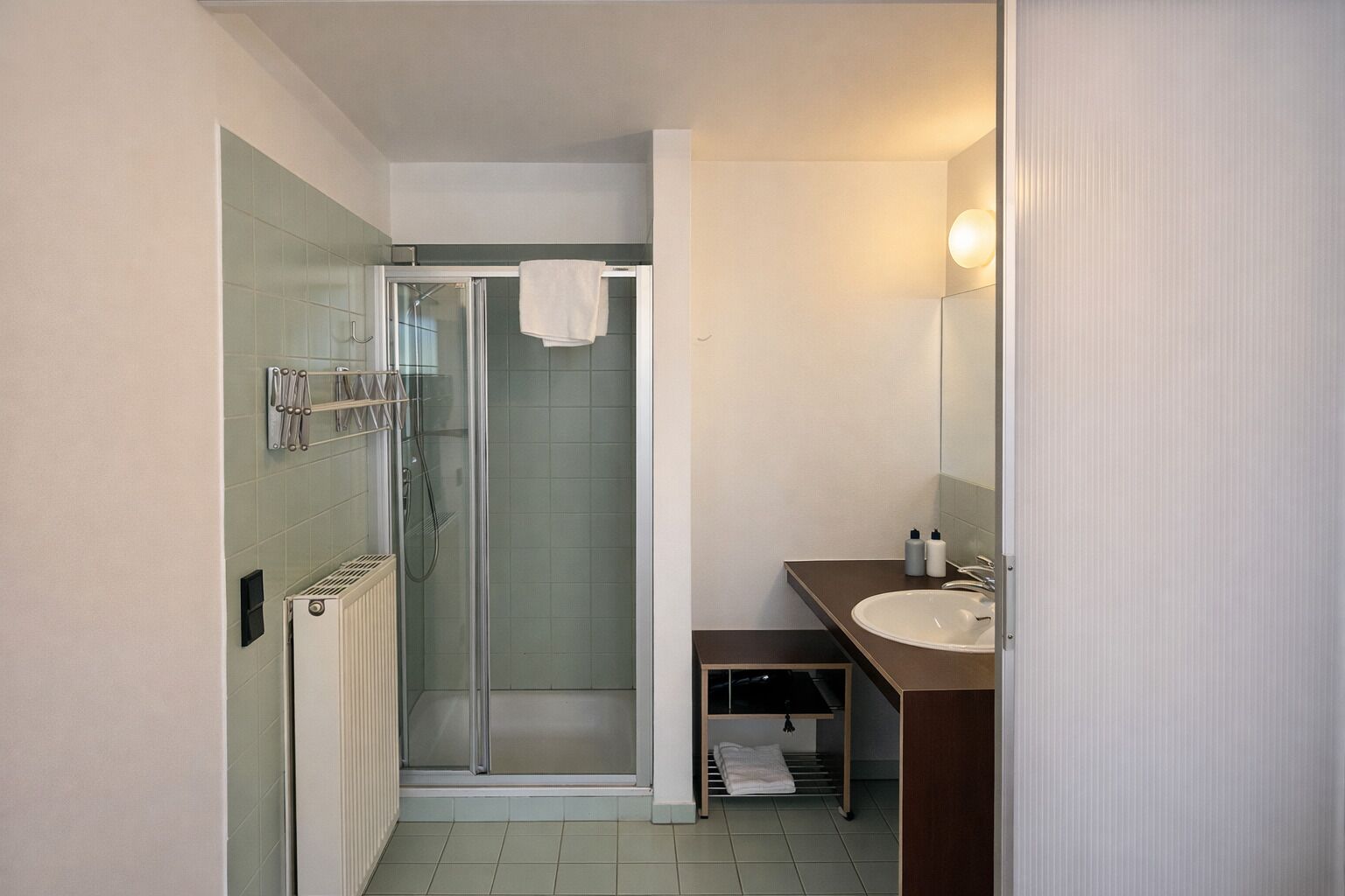 Un baño moderno con ducha de vidrio, un lavamanos y un perchero para toallas.