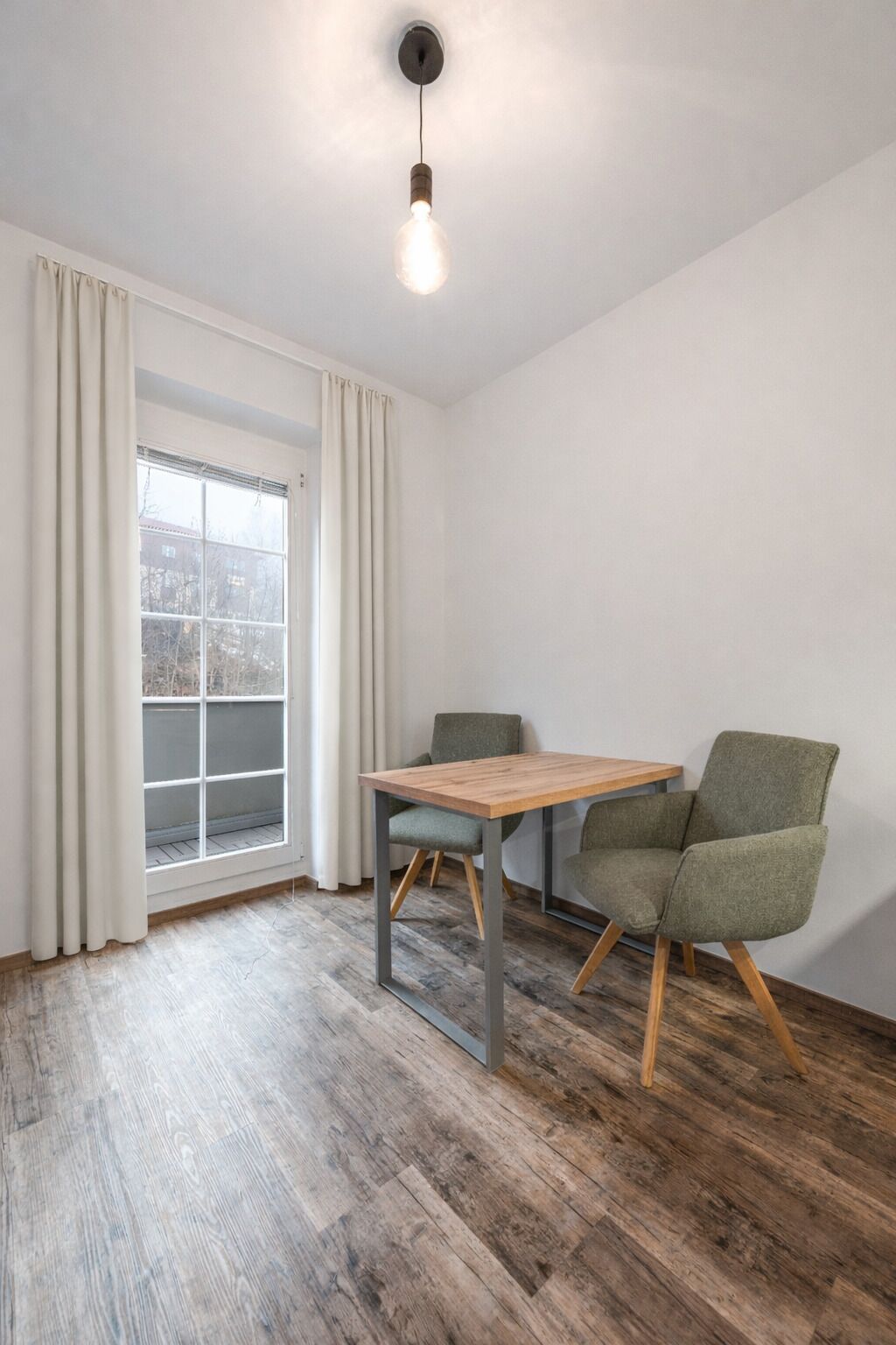 Une pièce moderne avec une table en bois et deux chaises vertes, une fenêtre avec des rideaux et un luminaire suspendu.