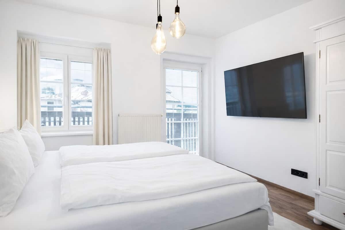 Ein modernes Hotelzimmer mit einem großen Bett, einem Flachbildfernseher und Blick auf die Stadt durch die Fenster.