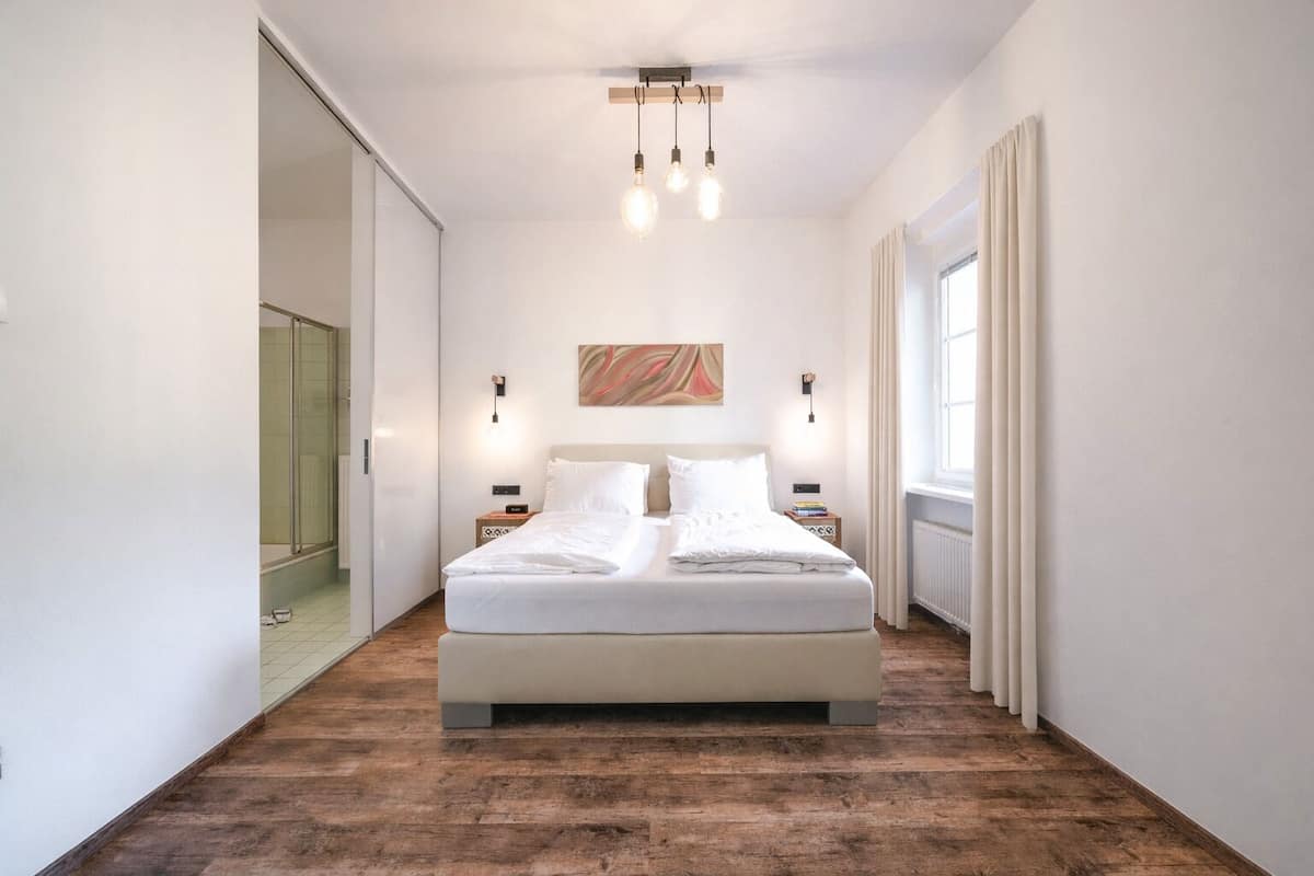 Ein modernes Schlafzimmer mit einem großen Bett, Holzboden, einer Glasdusche und Blick ins Freie.