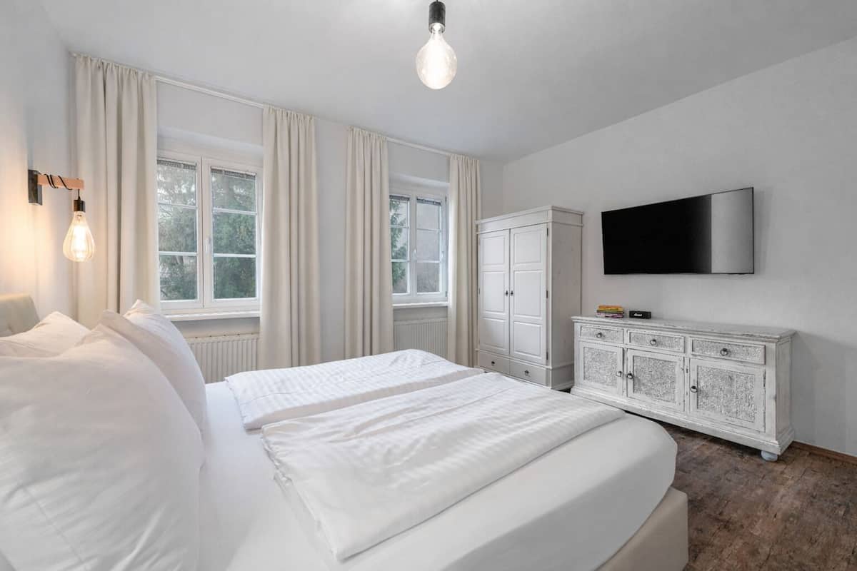Ein Schlafzimmer mit einem großen Bett, einem Kleiderschrank, einem Fernseher und einem Fenster mit Vorhängen.