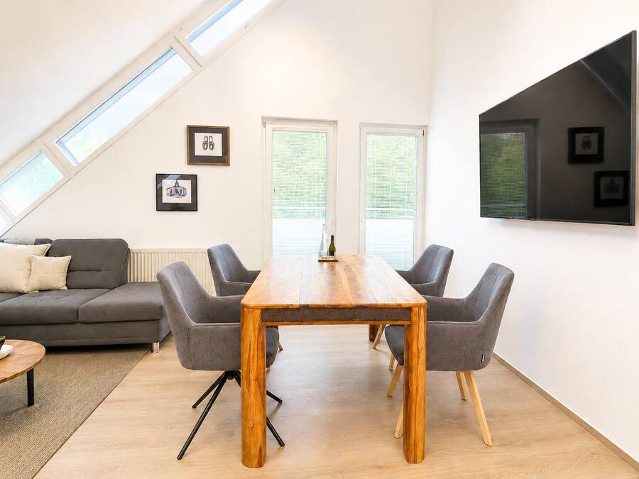 Una sala de estar moderna con una mesa de comedor de madera, sofás grises y un ventanal grande.