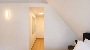 A bedroom with a sloped ceiling, a bed with white bedding, a nightstand, a lamp, and a framed picture on the wall.