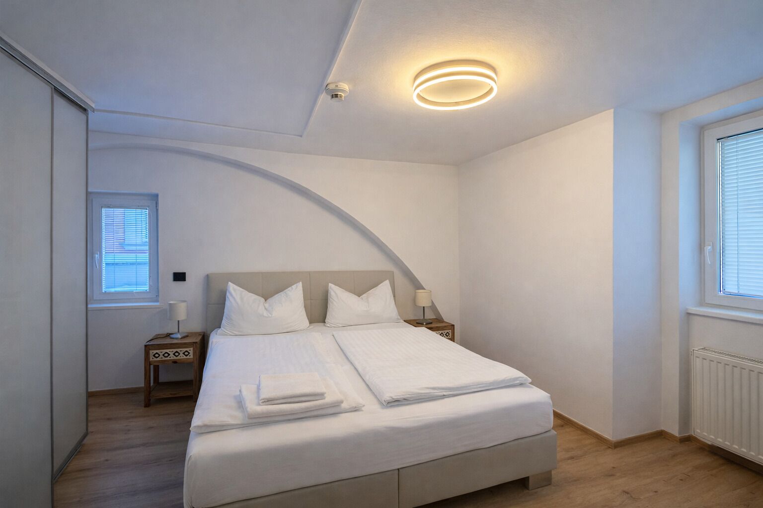 A bedroom with a bed, bedside tables, a window, and a ceiling light fixture.