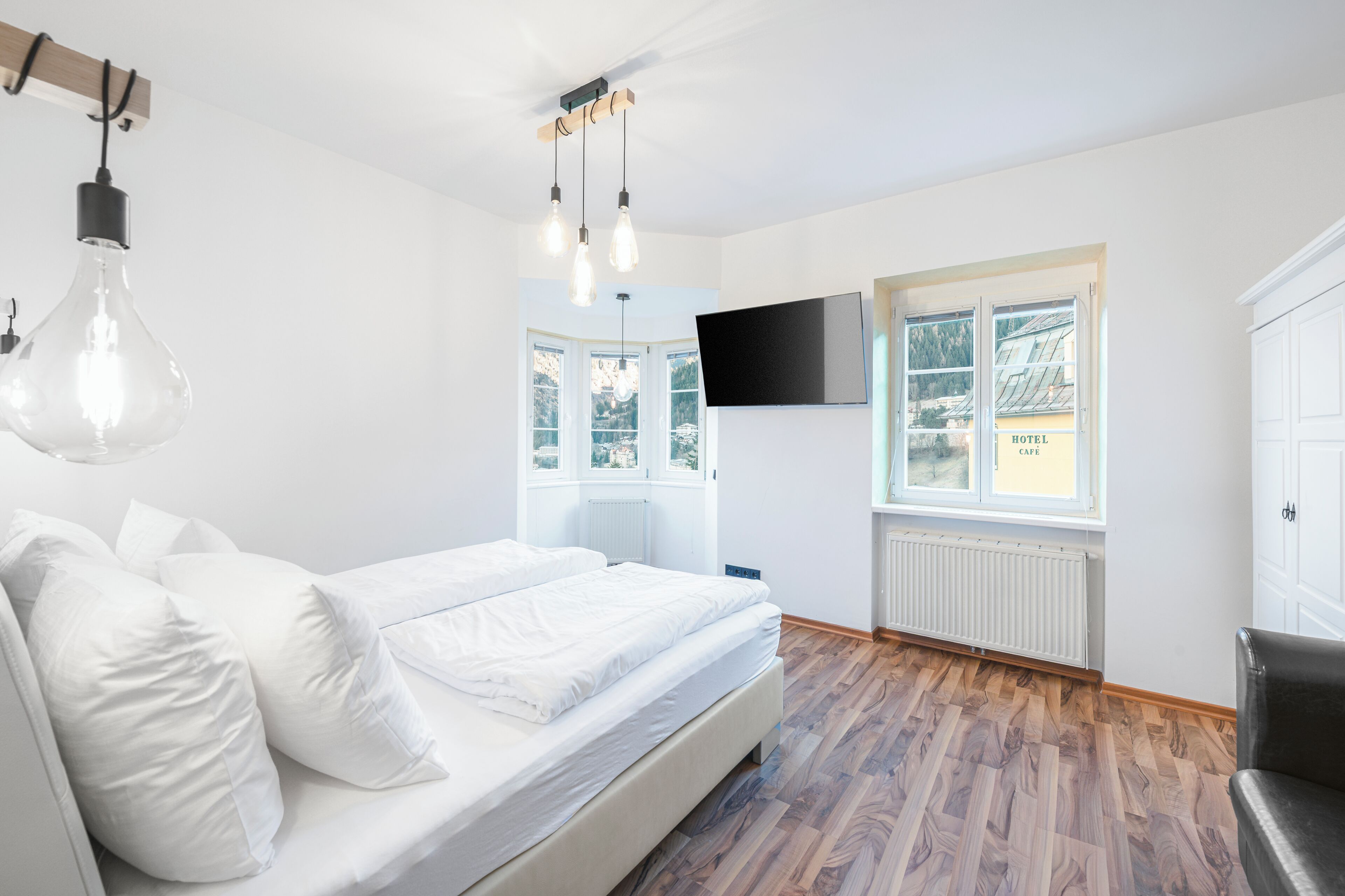Un dormitorio con cama, televisor montado en la pared y ventana con vistas al exterior.