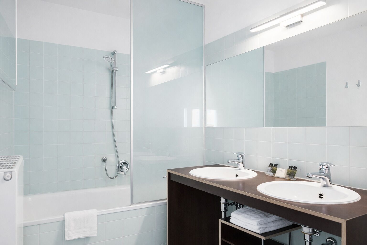 A modern bathroom with two sinks, a glass shower enclosure, and a large mirror.