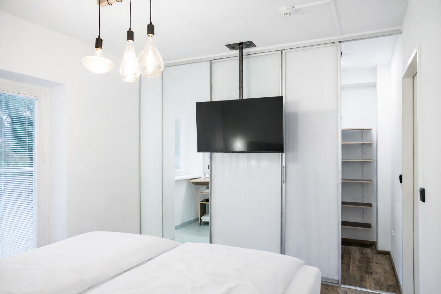 A modern bedroom with a bed, a TV mounted on a sliding door, and a closet with shelves.